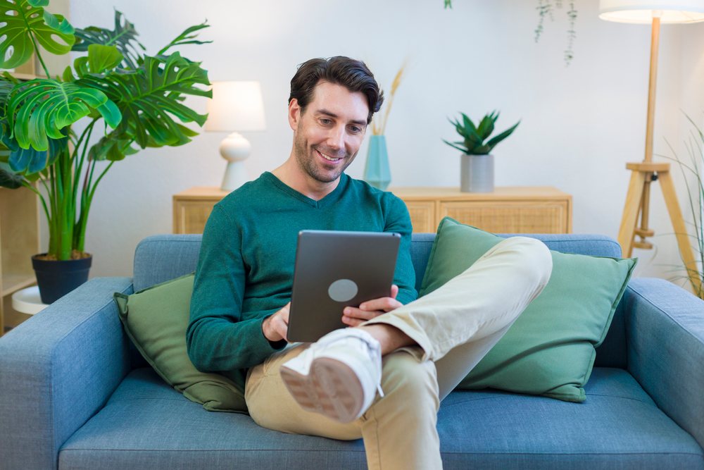 White man sitting on sofa using tablet in modern living room