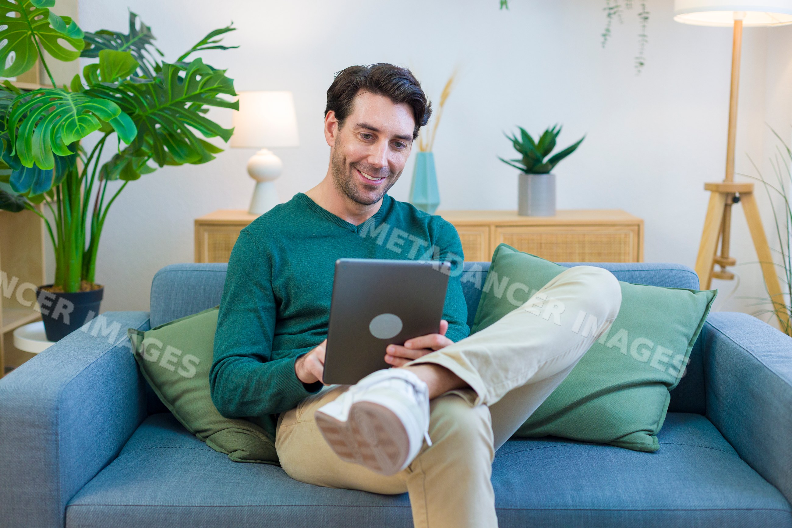 White man sitting on sofa using tablet in modern living room