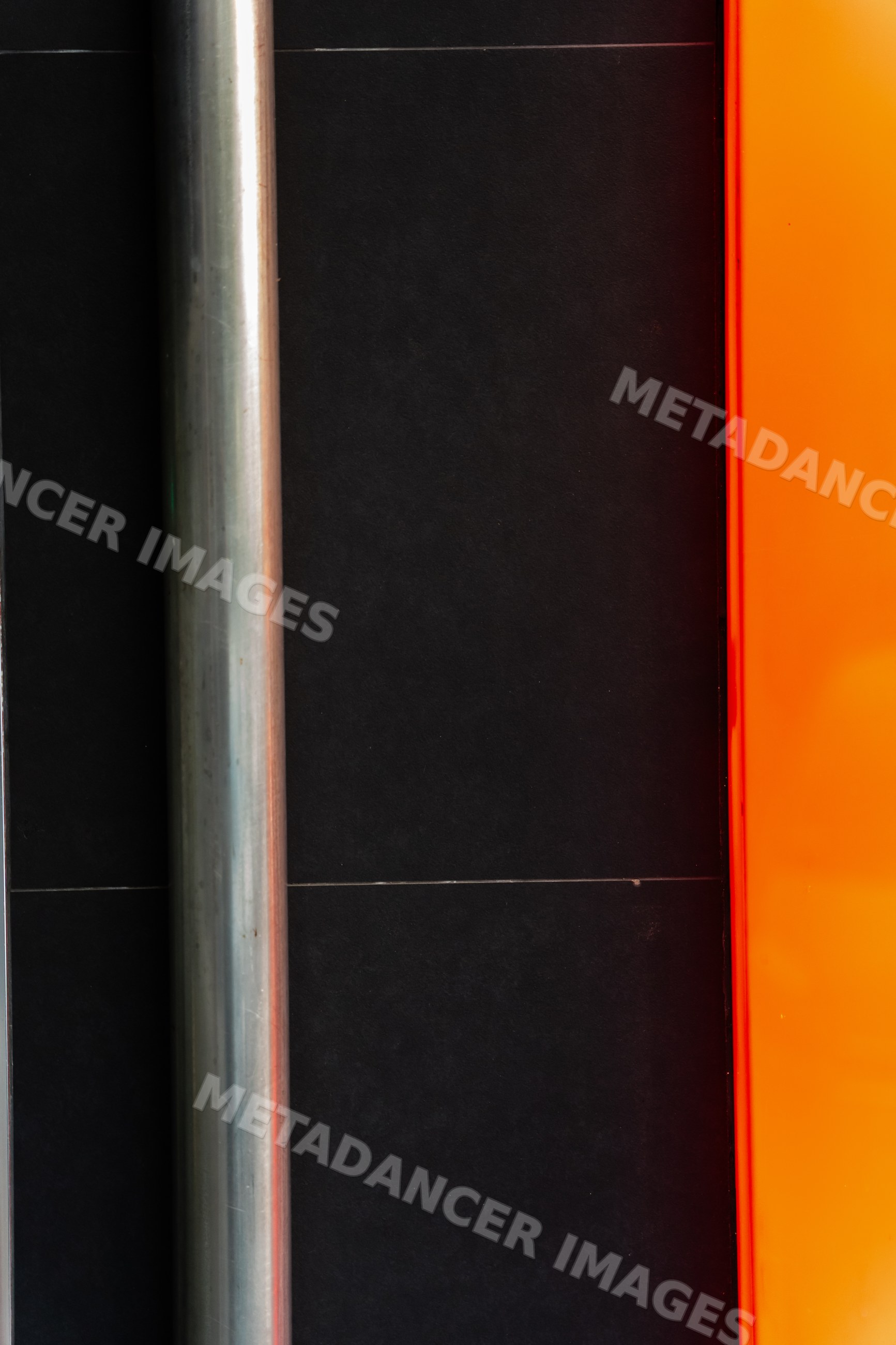 Vertical metal pipe mounted on black wall with orange panel contrast