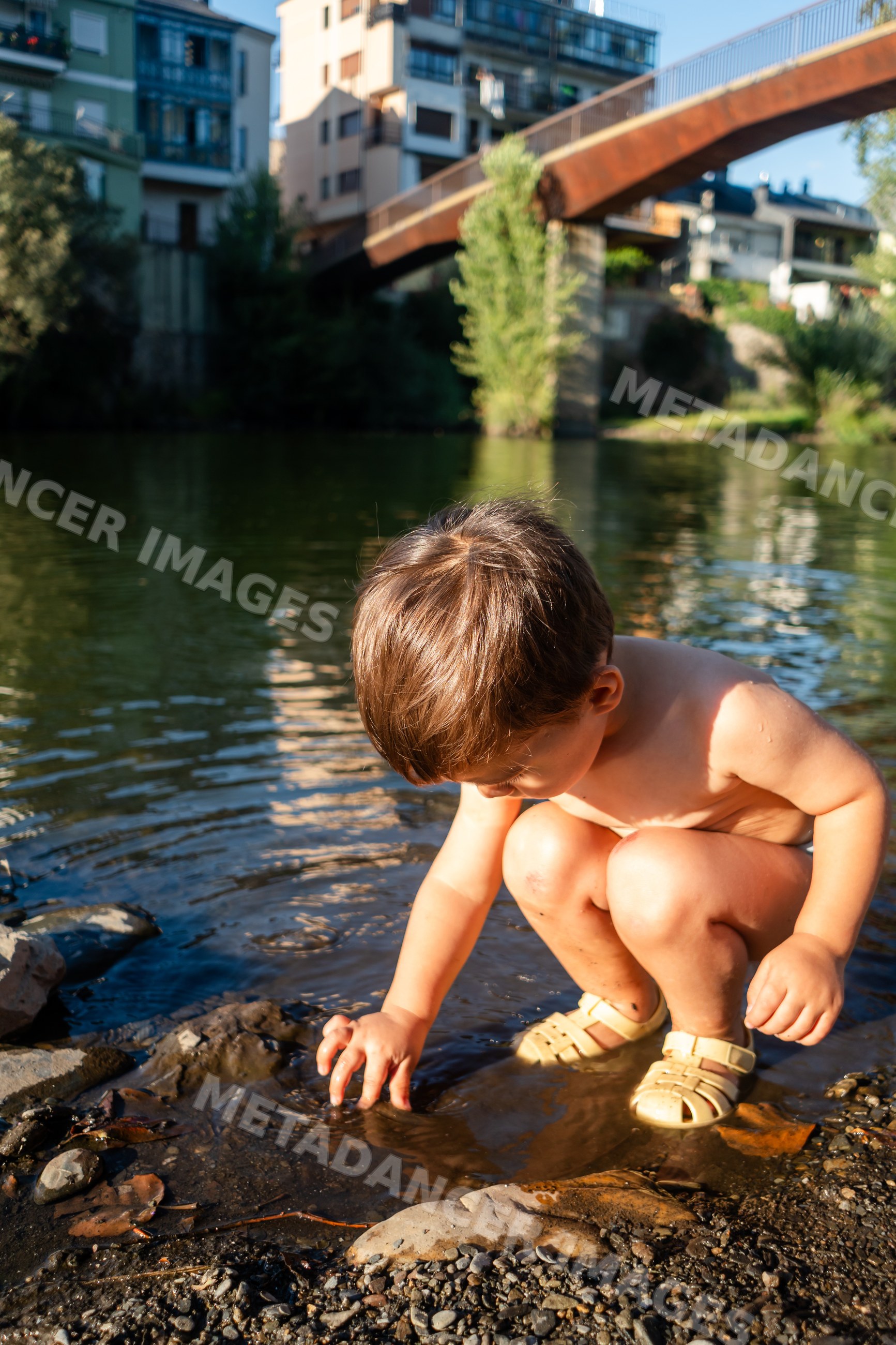 A young white boy playing with water and rocks at a riverbank in Spain