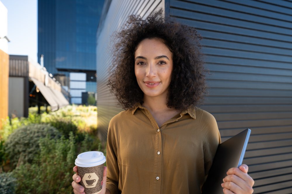 Woman holding coffee cup and laptop outdoors in urban environment