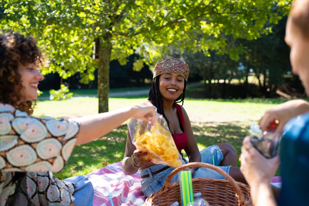 Friends enjoying a sunny picnic with chips and drinks in a park