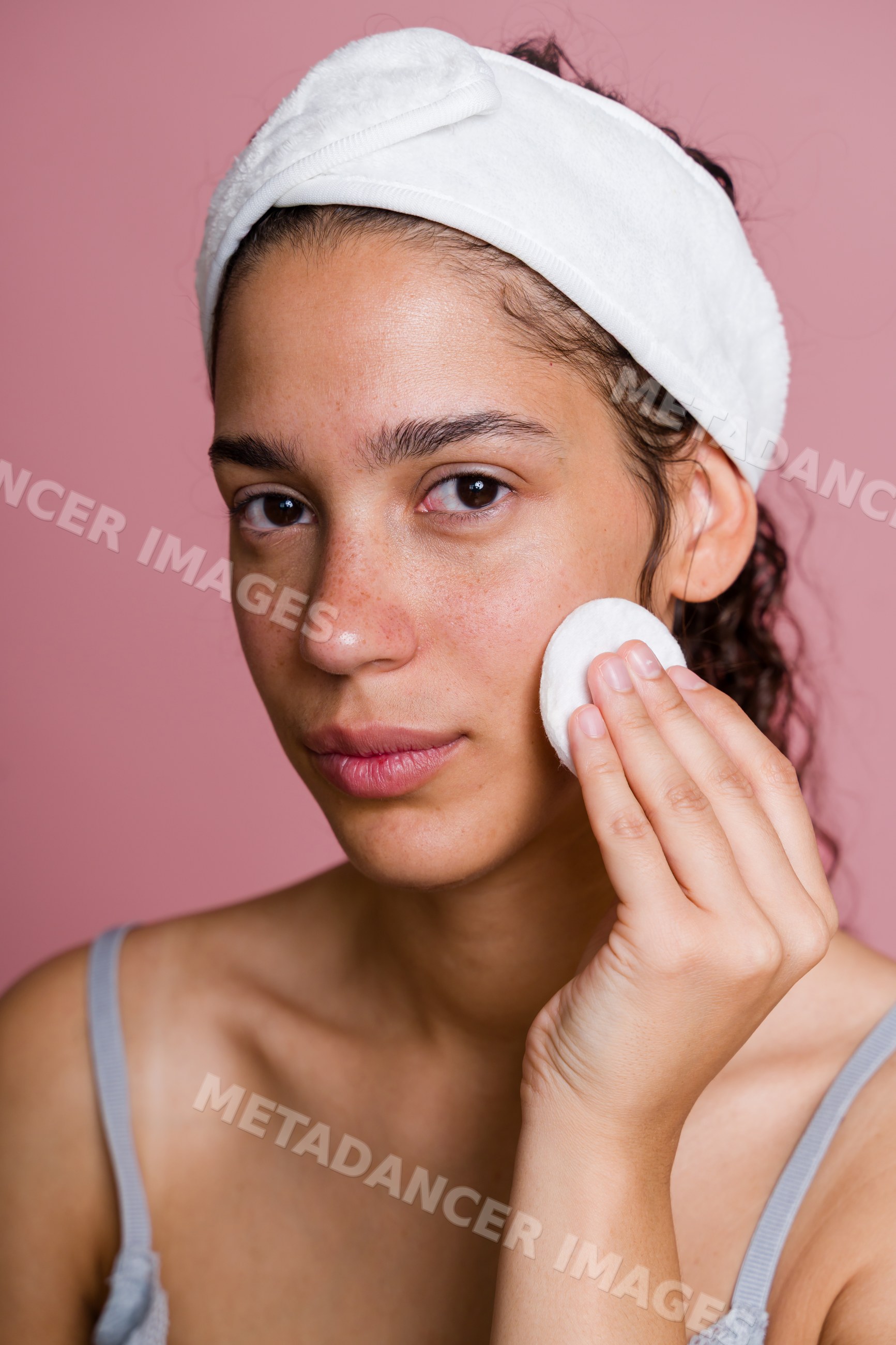 Hispanic woman cleansing face with cotton pad in skincare routine