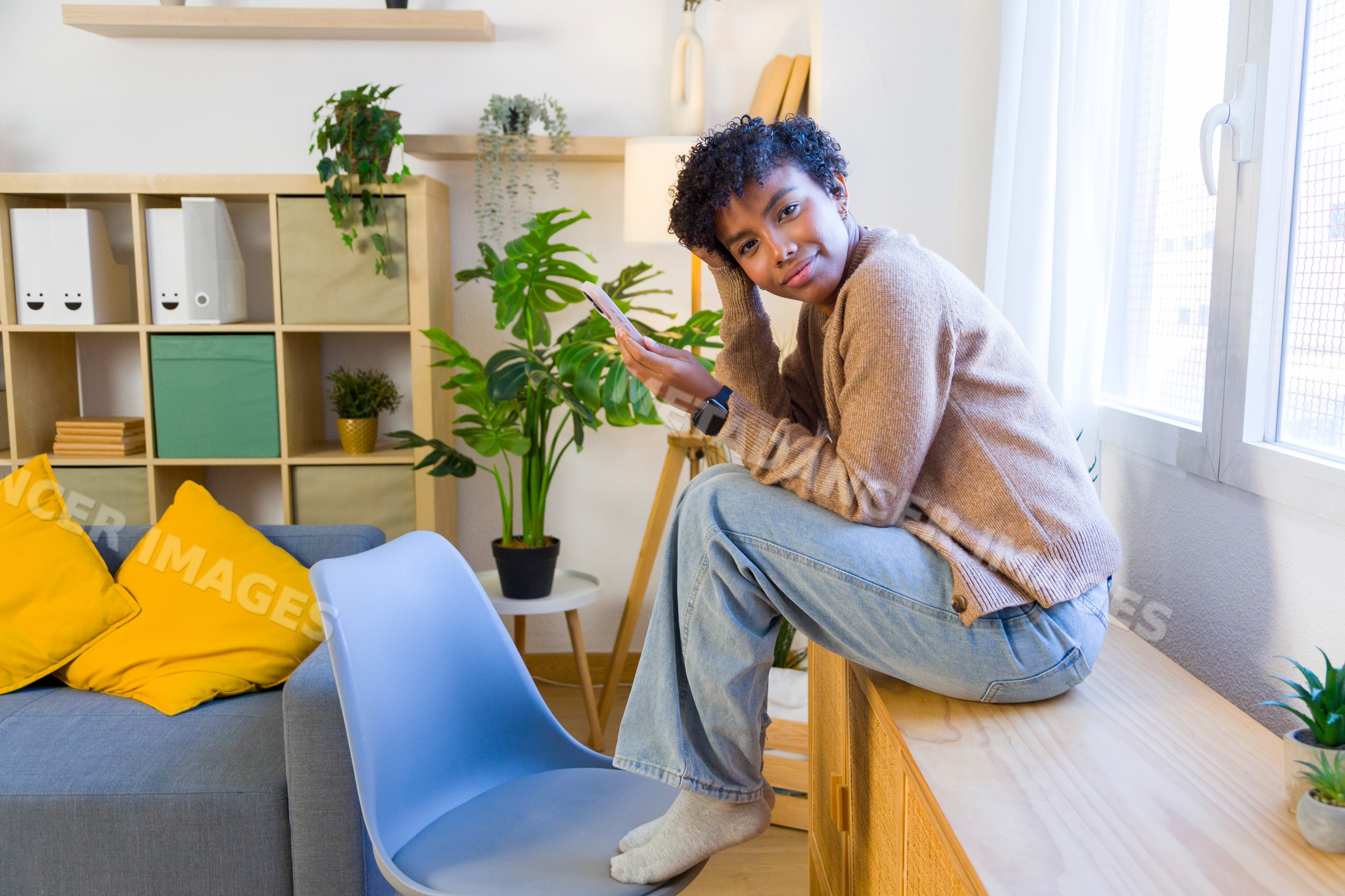 Young African American woman relaxing at home with phone near window