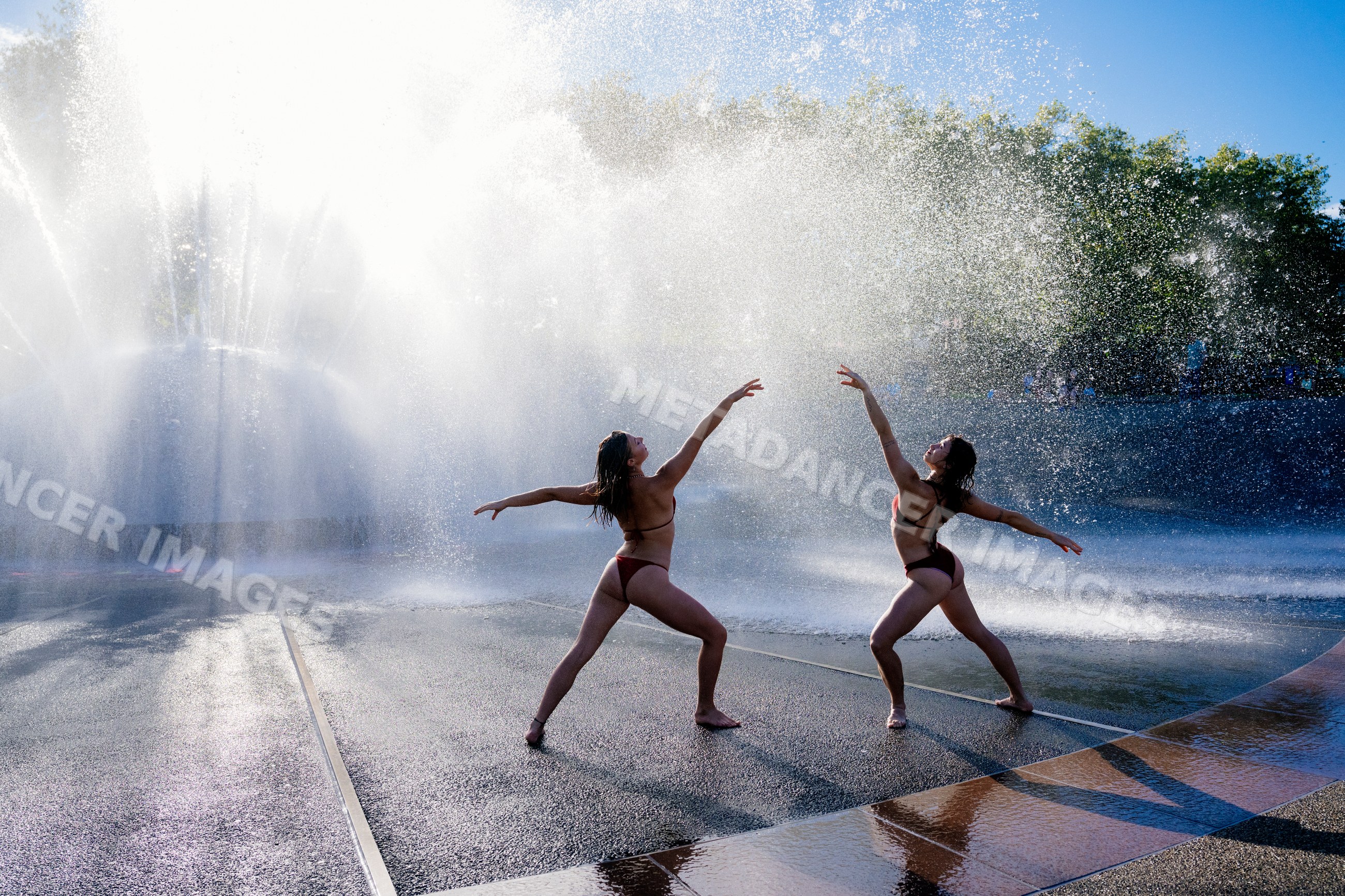 Partner yoga practice by fountain with water spray outdoors