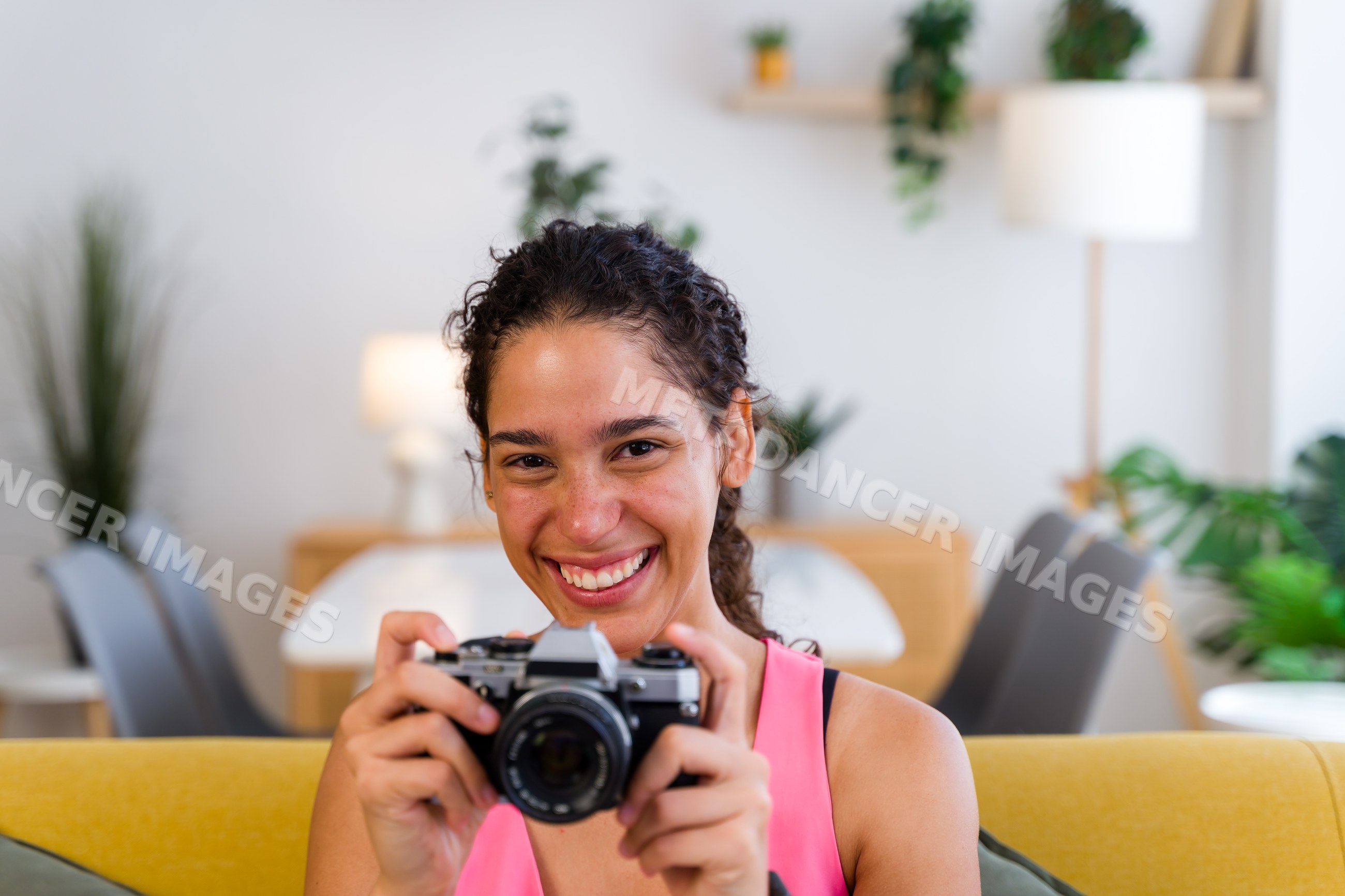 A Hispanic woman happily holding a camera in a modern living room