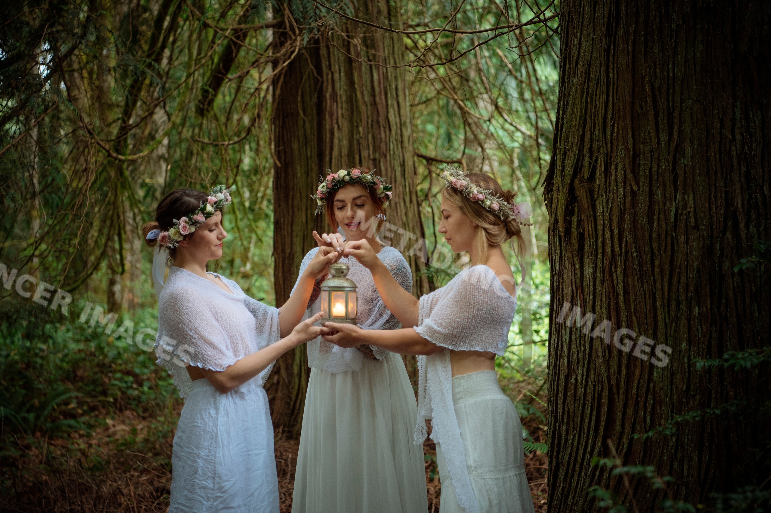 Three white women in flower crowns holding lantern in forest
