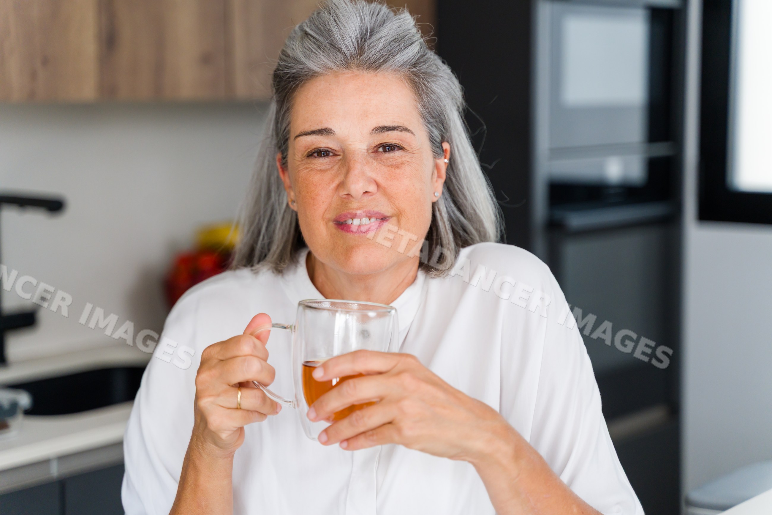 Mature white woman drinking tea in a kitchen interior in a kitchen