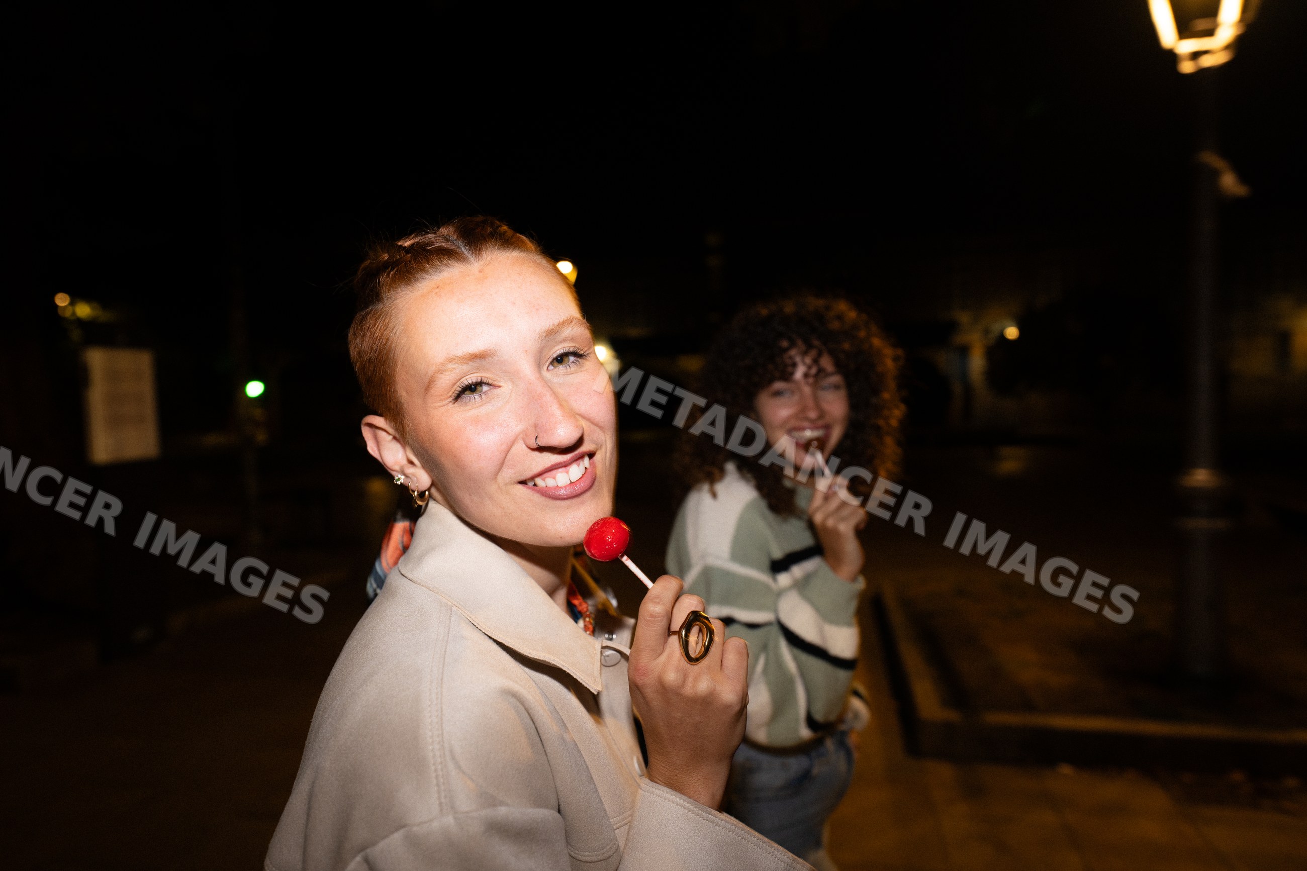 Two white women enjoying lollipops at night in a street