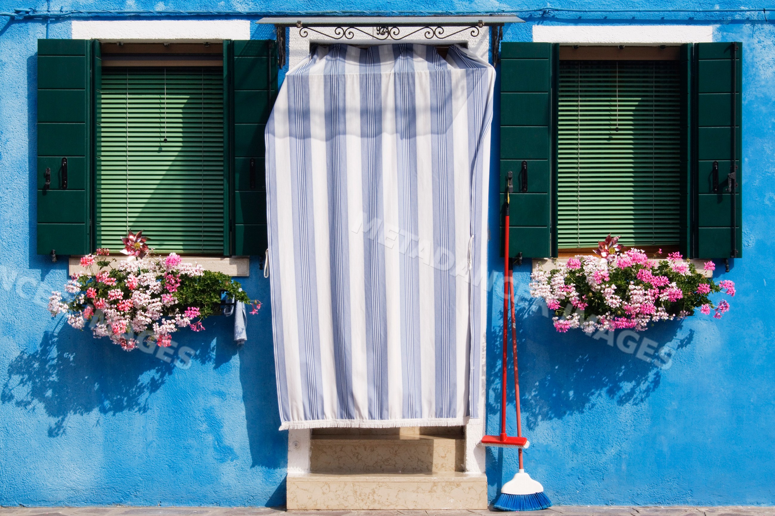 Doorway with striped curtain and flower boxes on blue building italy