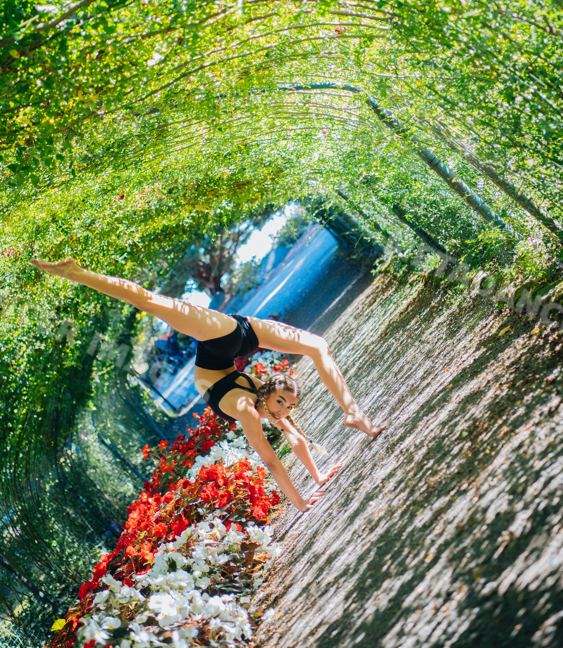 Contortionist doing handstand under garden arch beside flowers