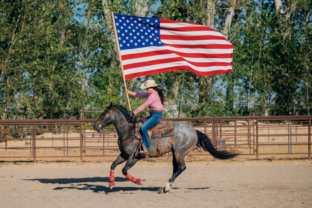 White woman riding horse holding american flag in rodeo arena
