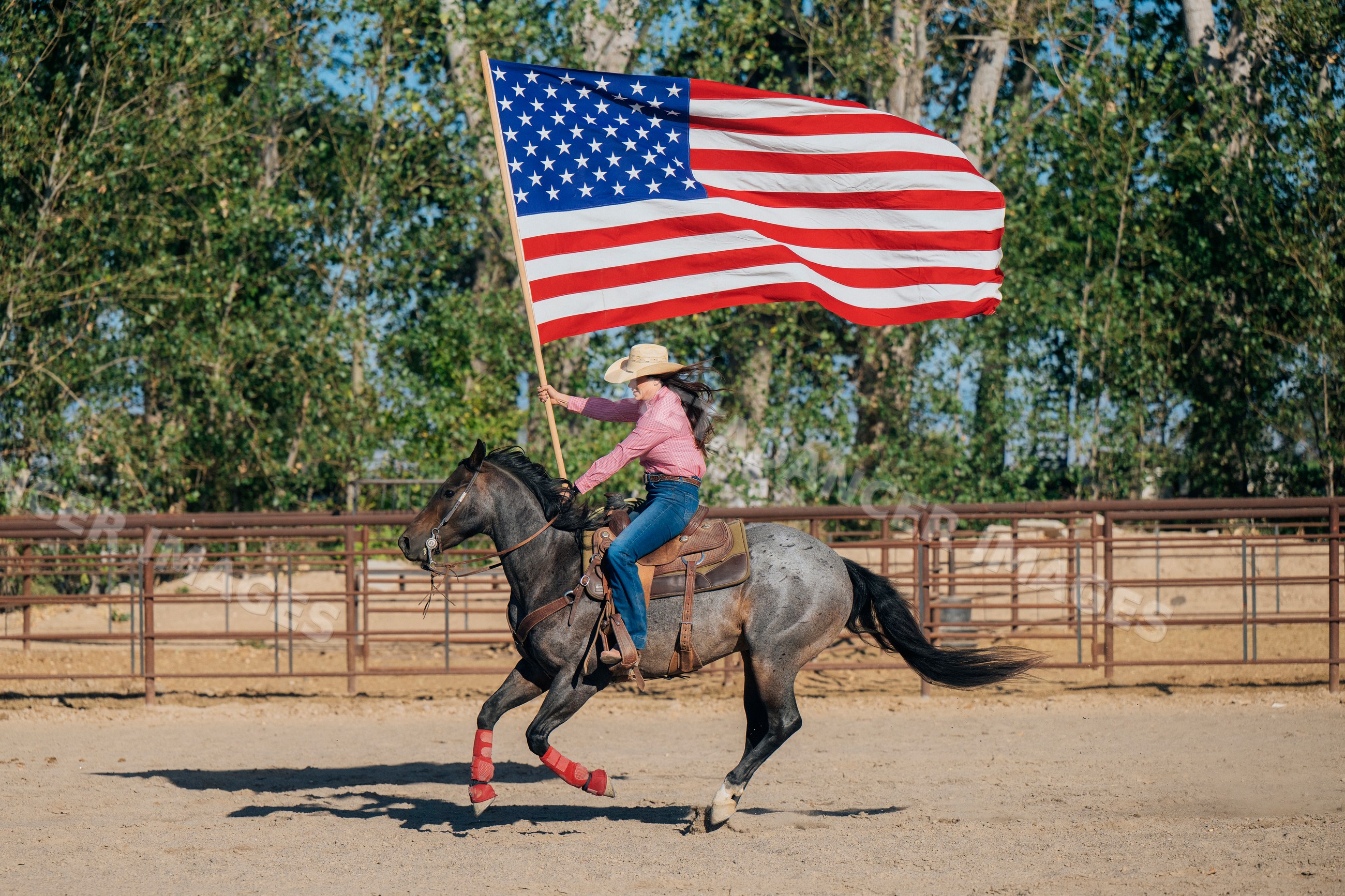 White woman riding horse holding american flag in rodeo arena