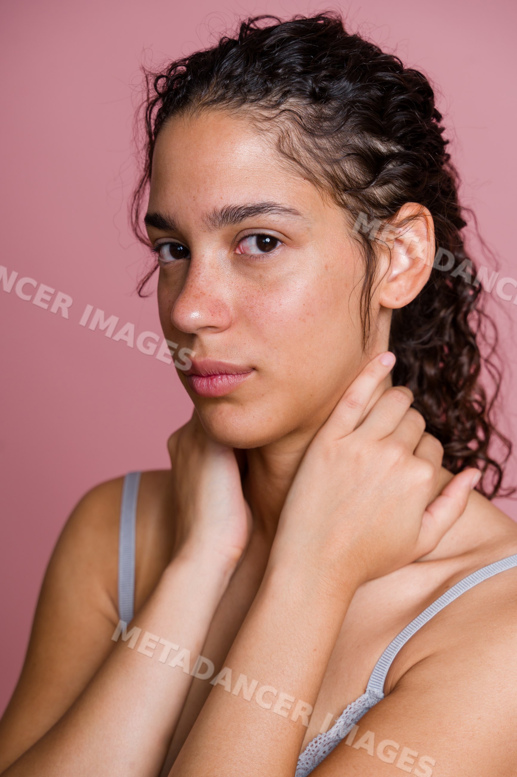 Portrait of young Hispanic woman with curly hair against pink