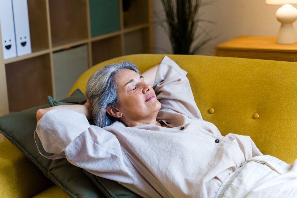 White woman relaxing with eyes closed on yellow sofa indoors