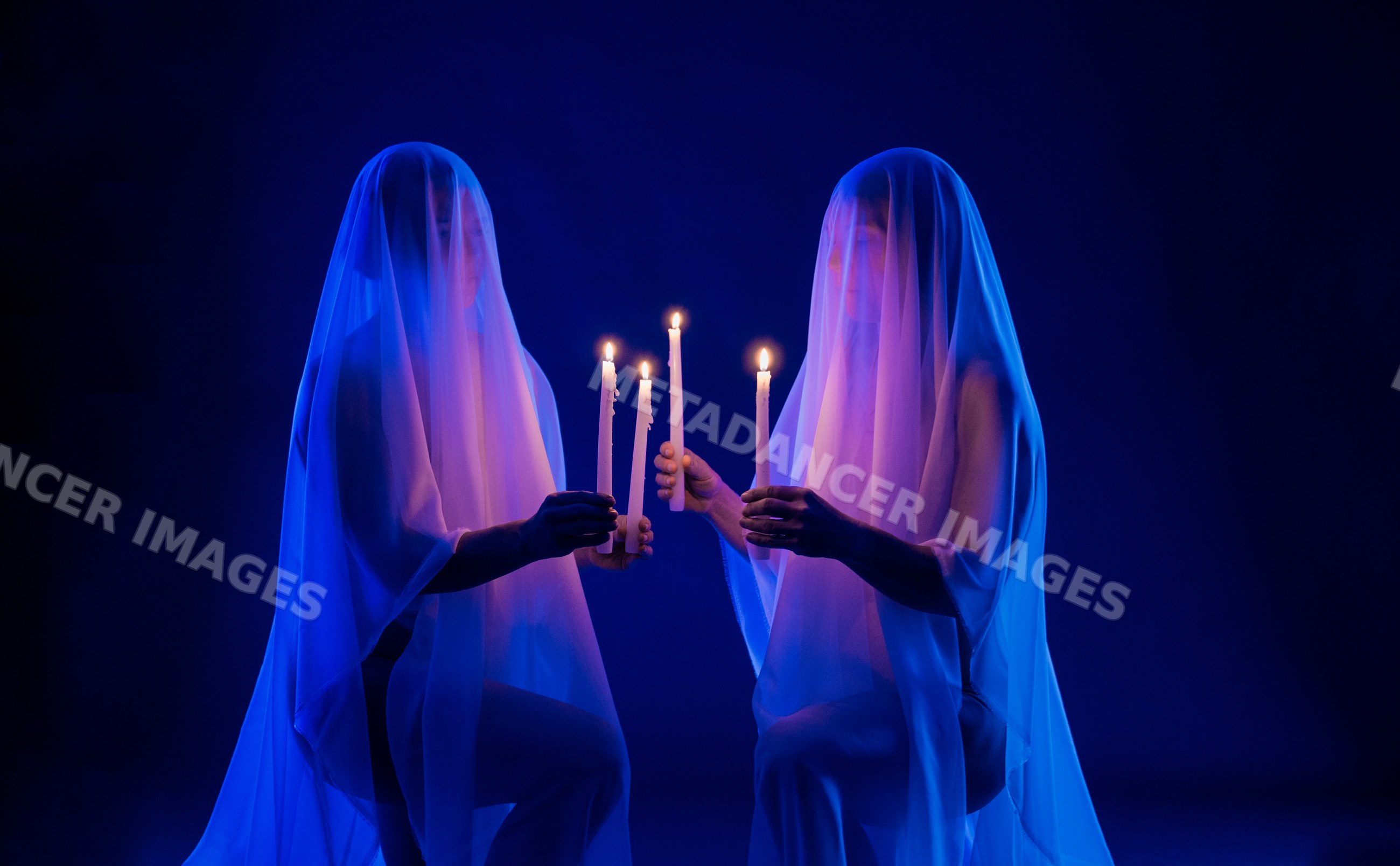Two people holding lit candles under white veils in blue light