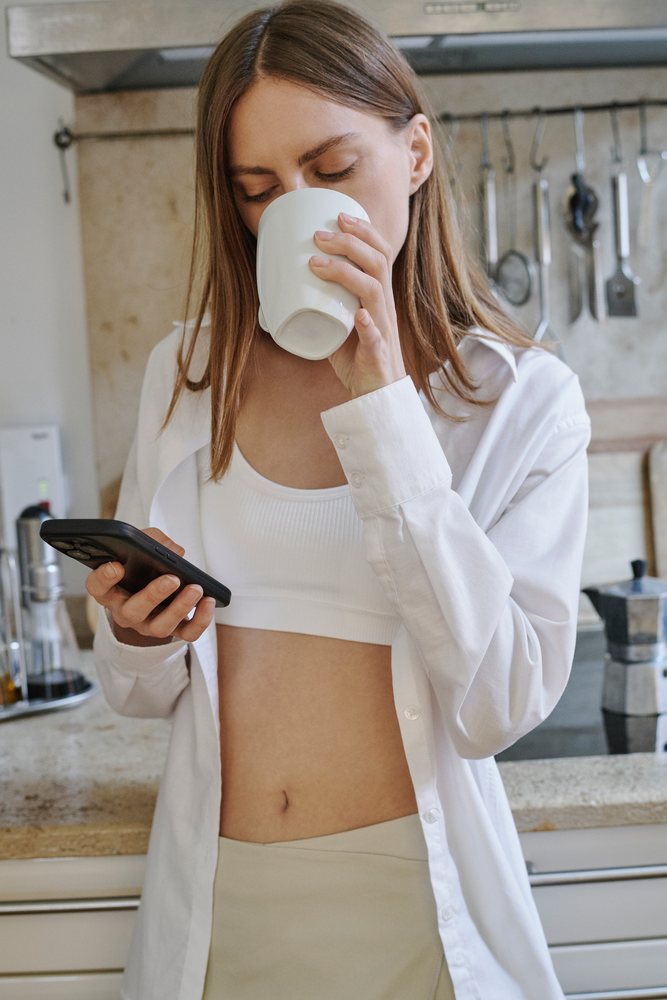 A young white woman drinks coffee and texts on her smartphone