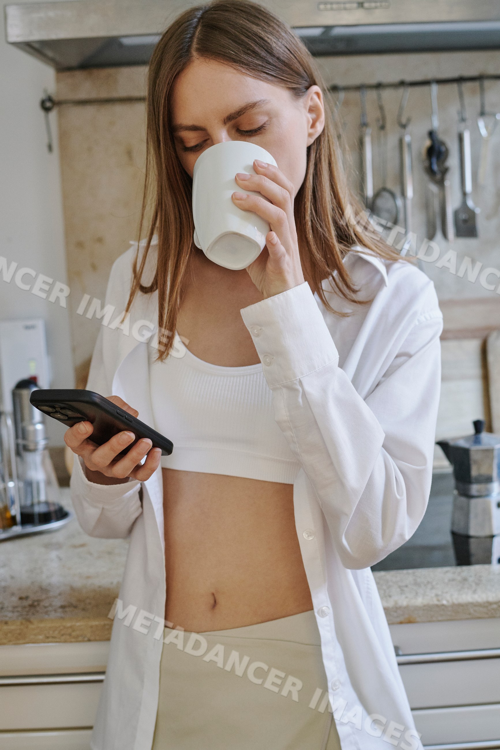 A young white woman drinks coffee and texts on her smartphone