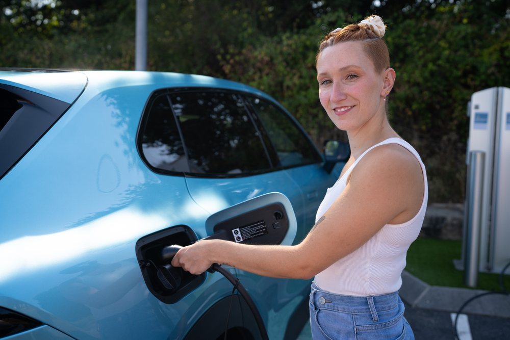 A white woman is charging her electric vehicle at a charging station