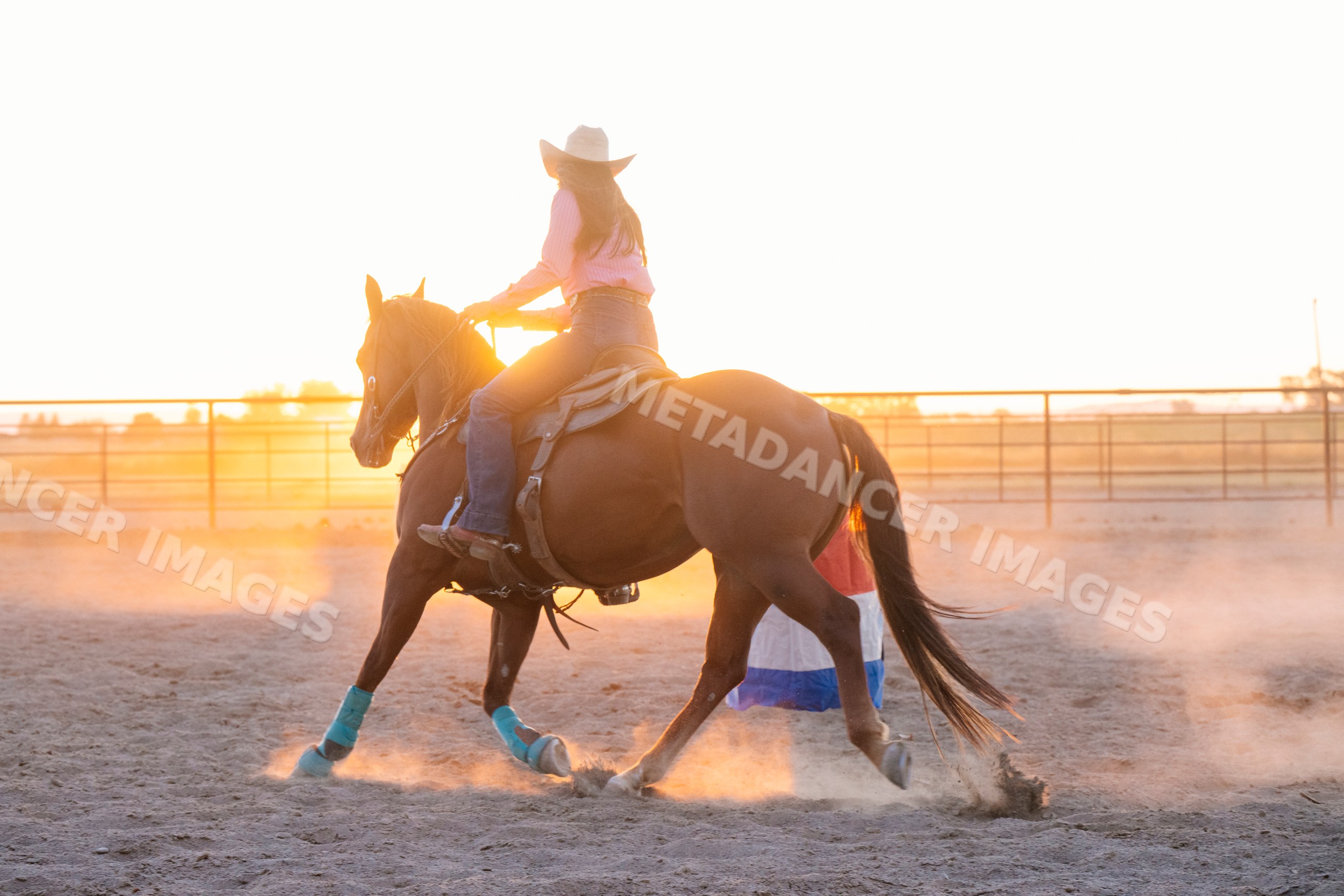 Cowgirl riding horse at sunset in dusty Southwest USA arena