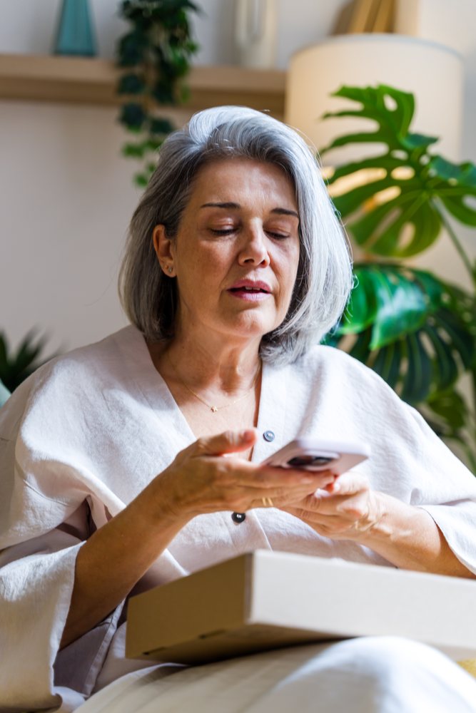 Senior white woman using smartphone indoors with cardboard box