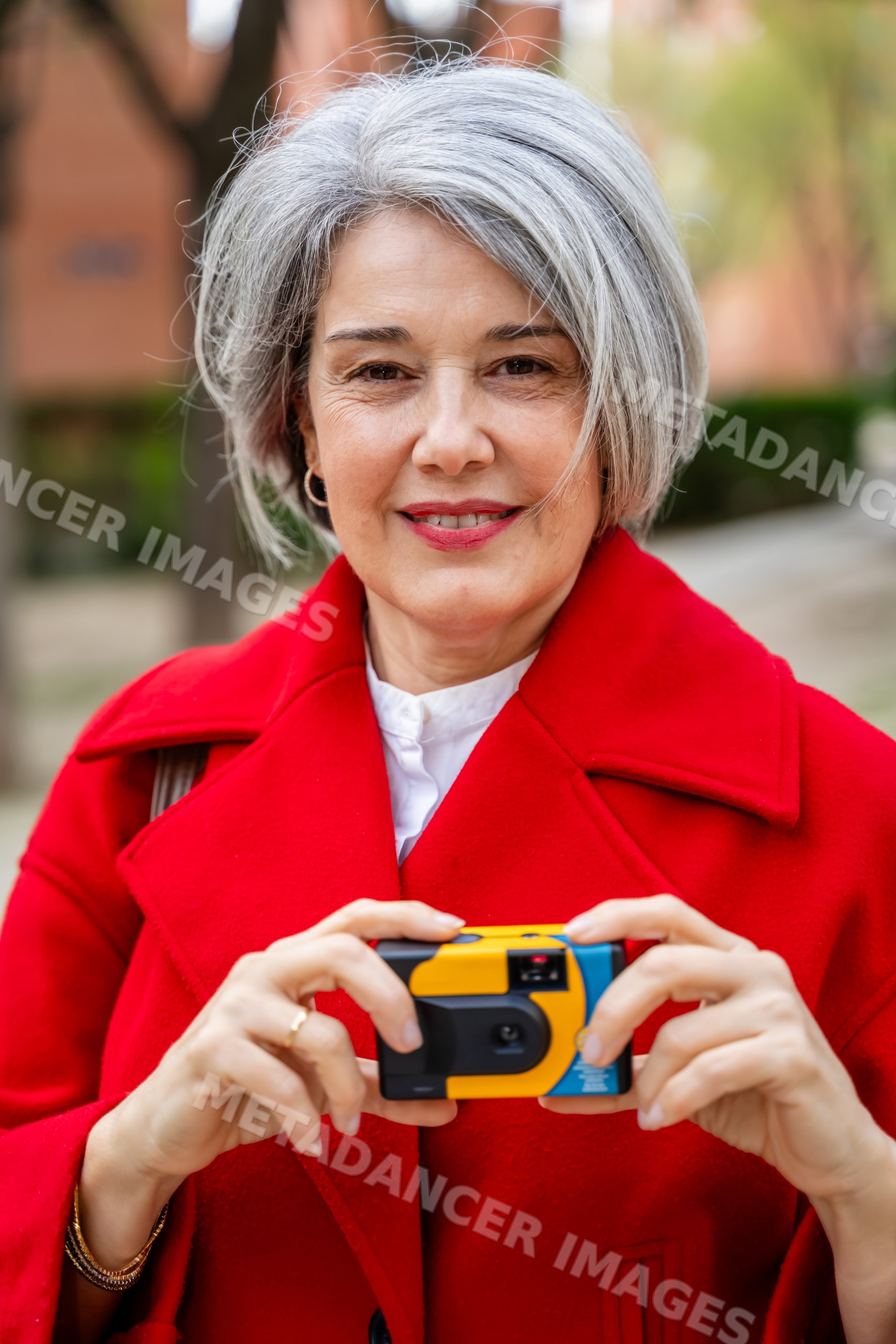 White woman holding camera outdoors in red coat in Spain