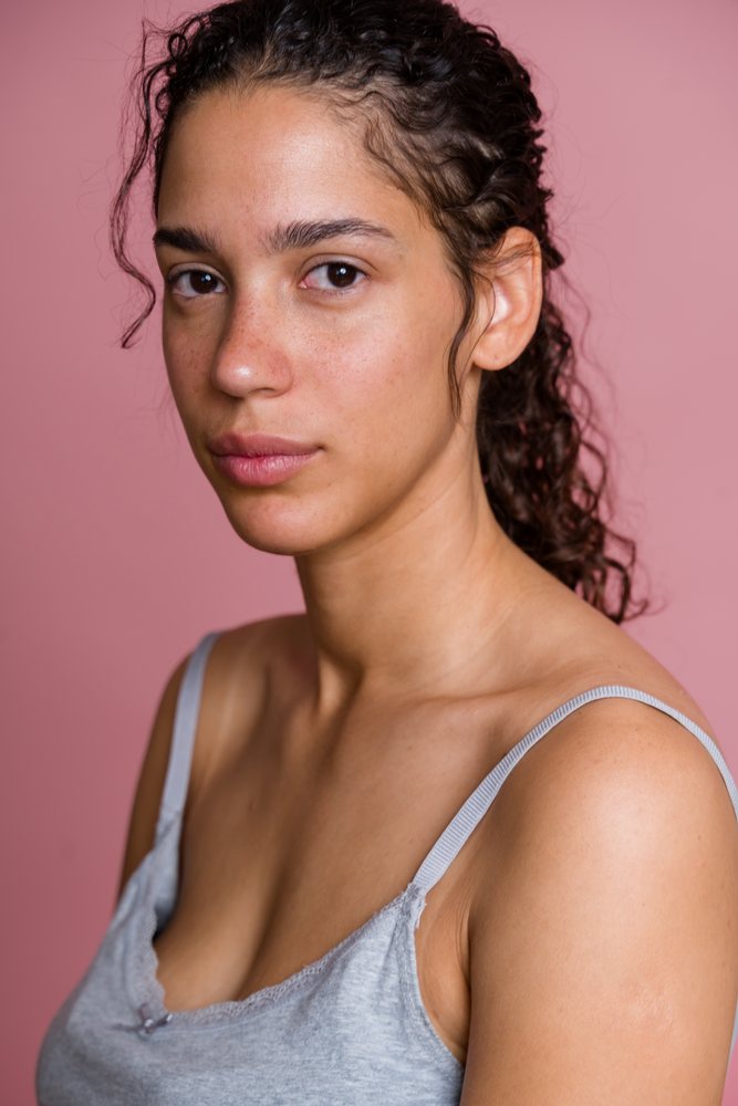 Portrait of Hispanic woman with curly hair against pink background