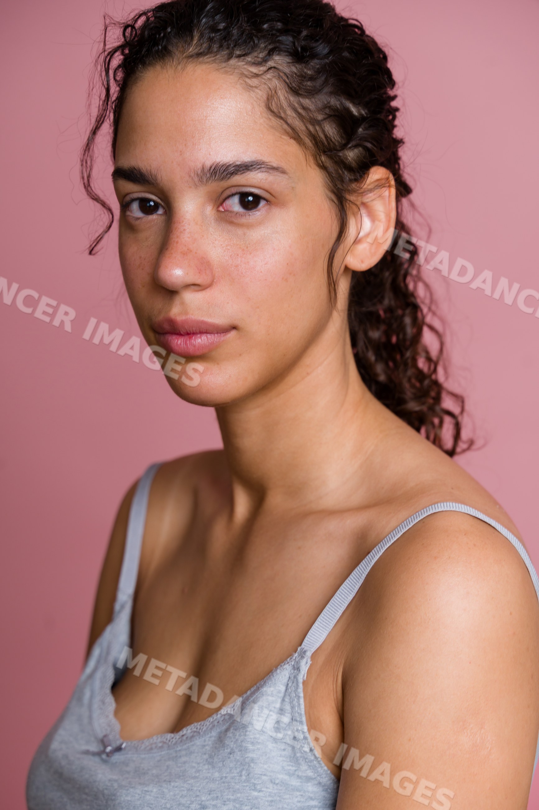 Portrait of Hispanic woman with curly hair against pink background