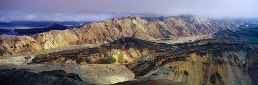 Aerial panoramic view of a mountain range with river valley and clouds