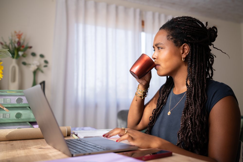 African American woman drinking coffee while working on her laptop