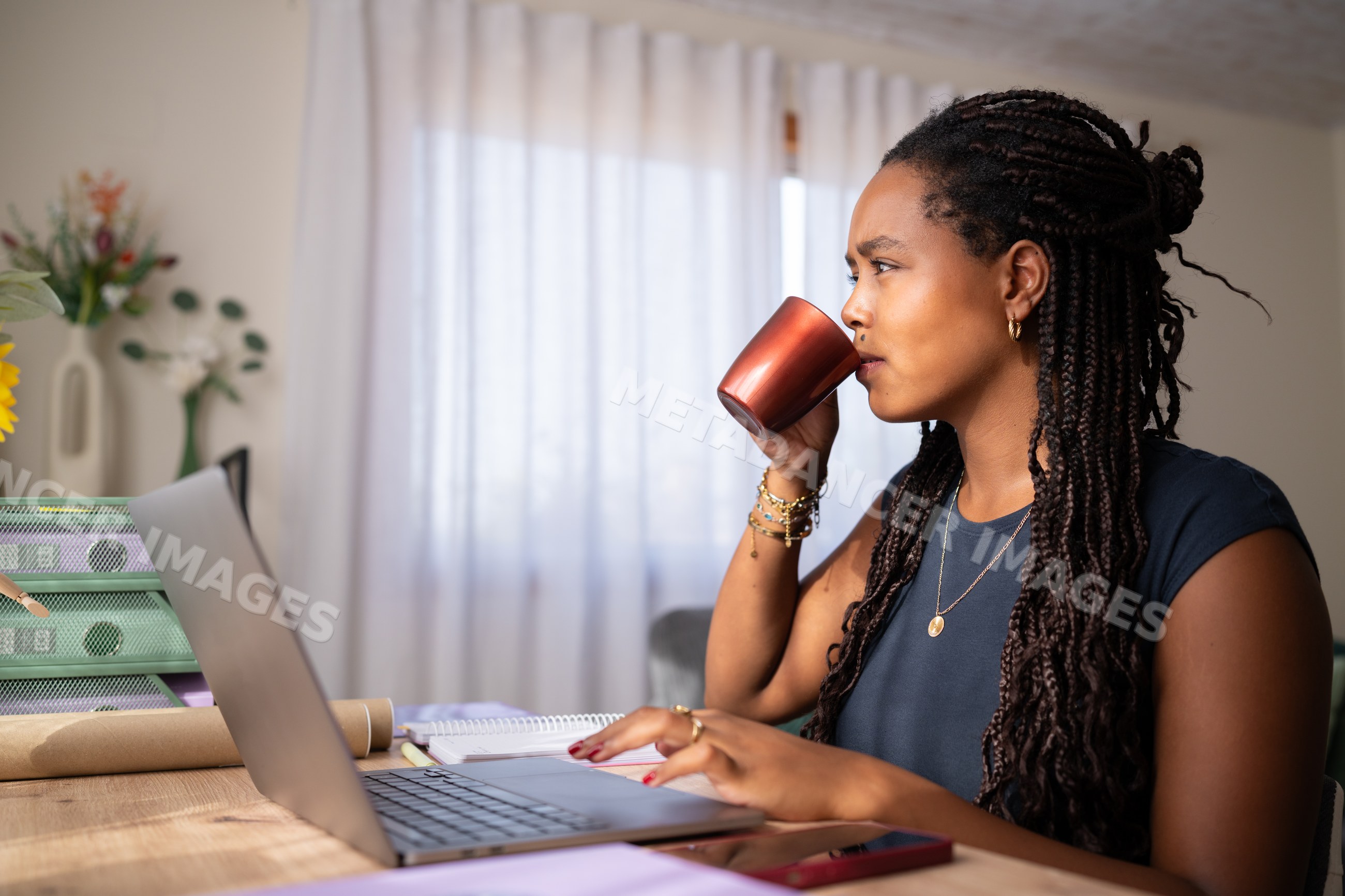 African American woman drinking coffee while working on her laptop