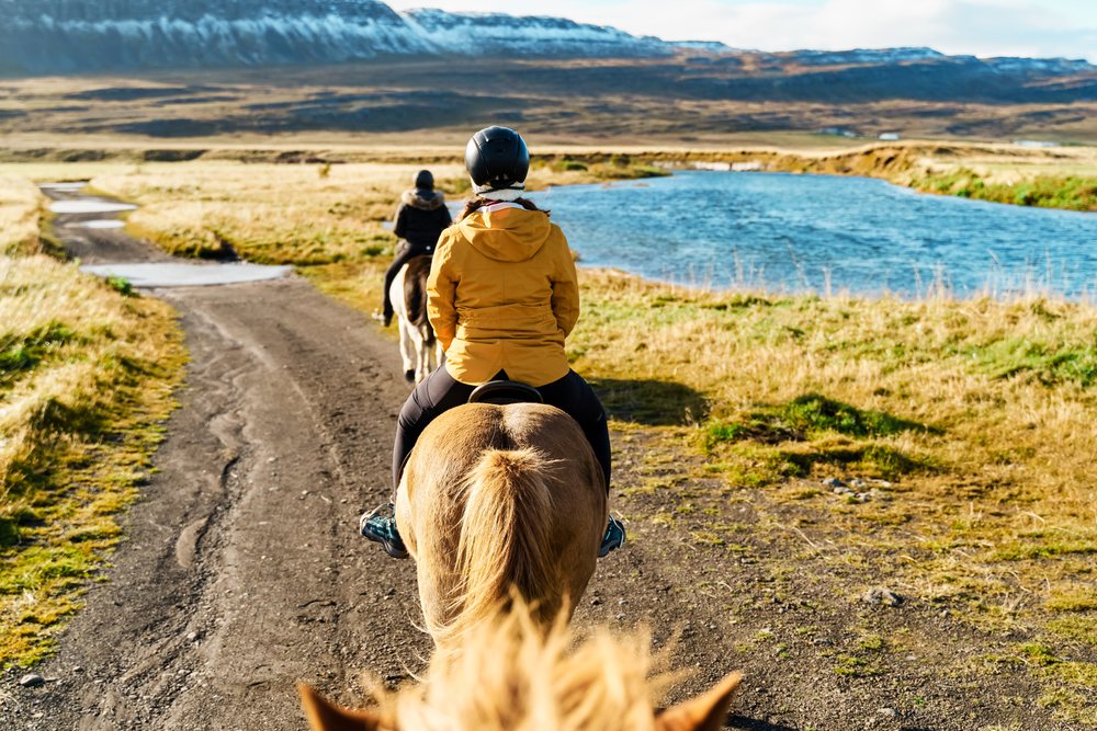 Two white women horseback riding on a trail beside a river