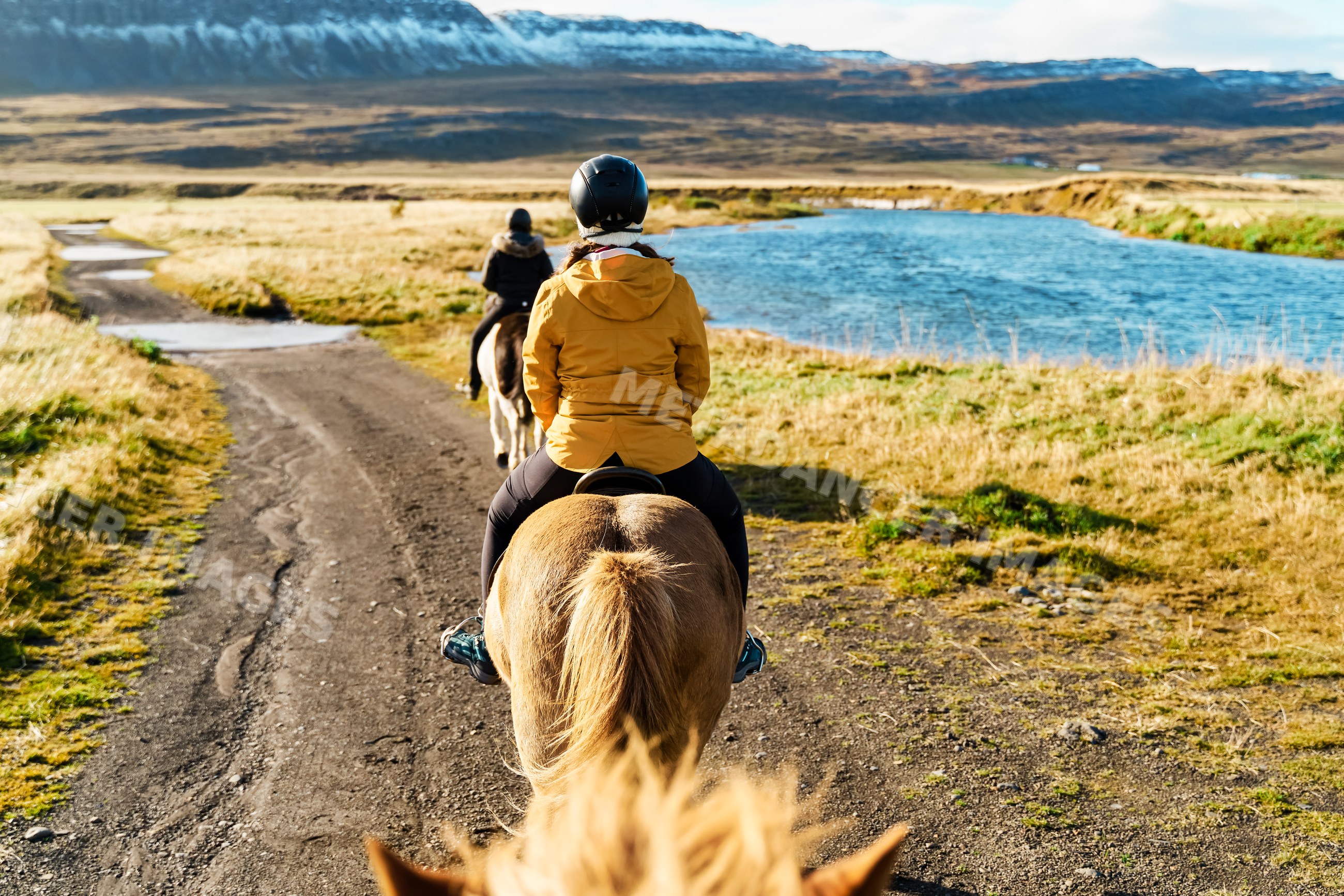 Two white women horseback riding on a trail beside a river