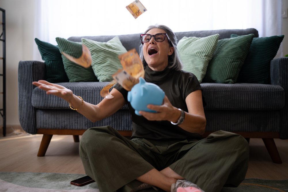 White woman sitting on floor throwing money with piggy bank indoors