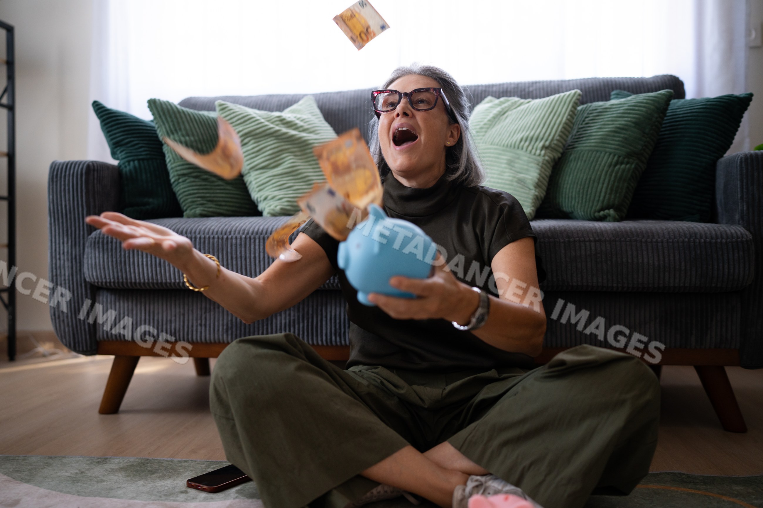 White woman sitting on floor throwing money with piggy bank indoors
