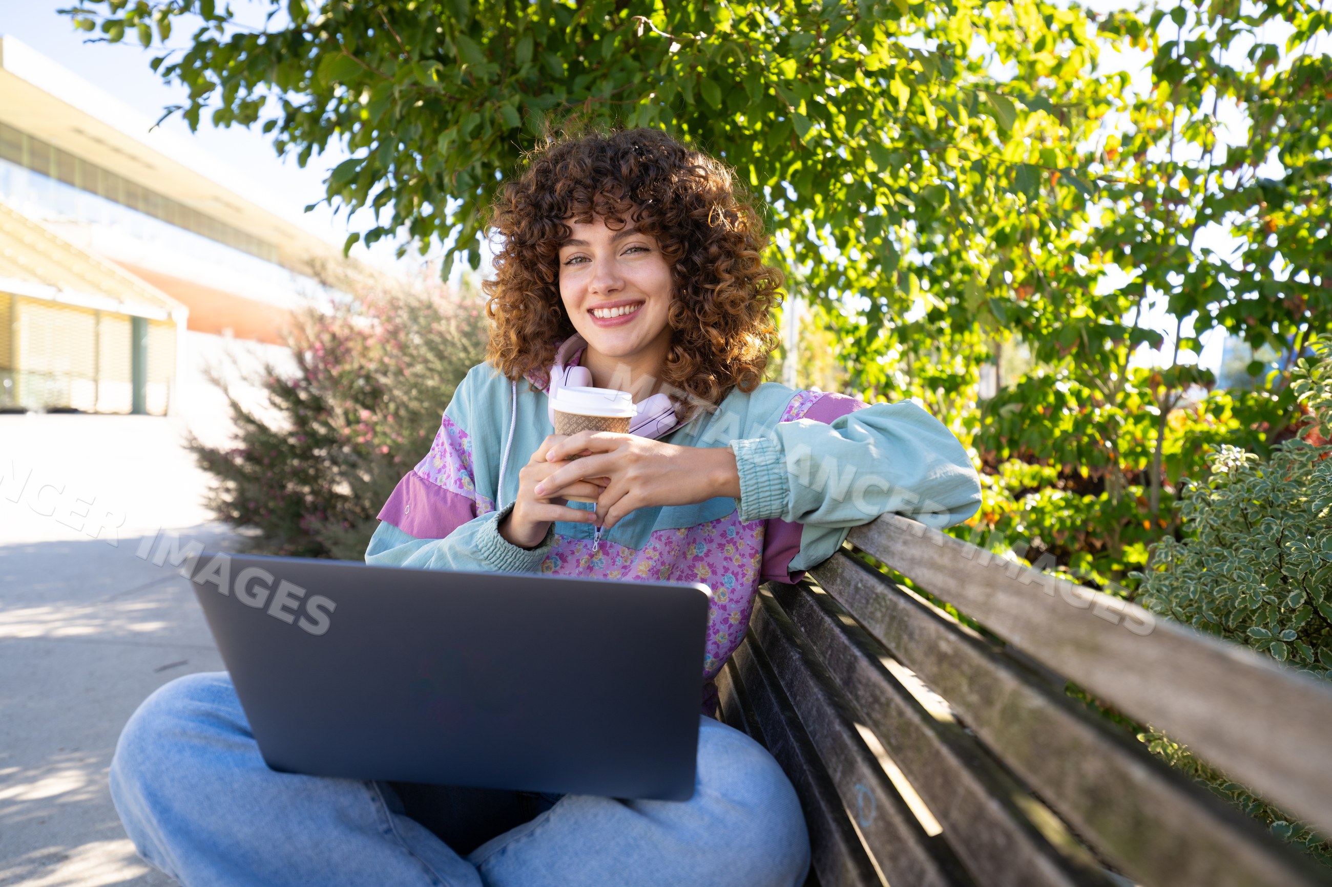 White woman sitting on bench outdoors with laptop and coffee cup