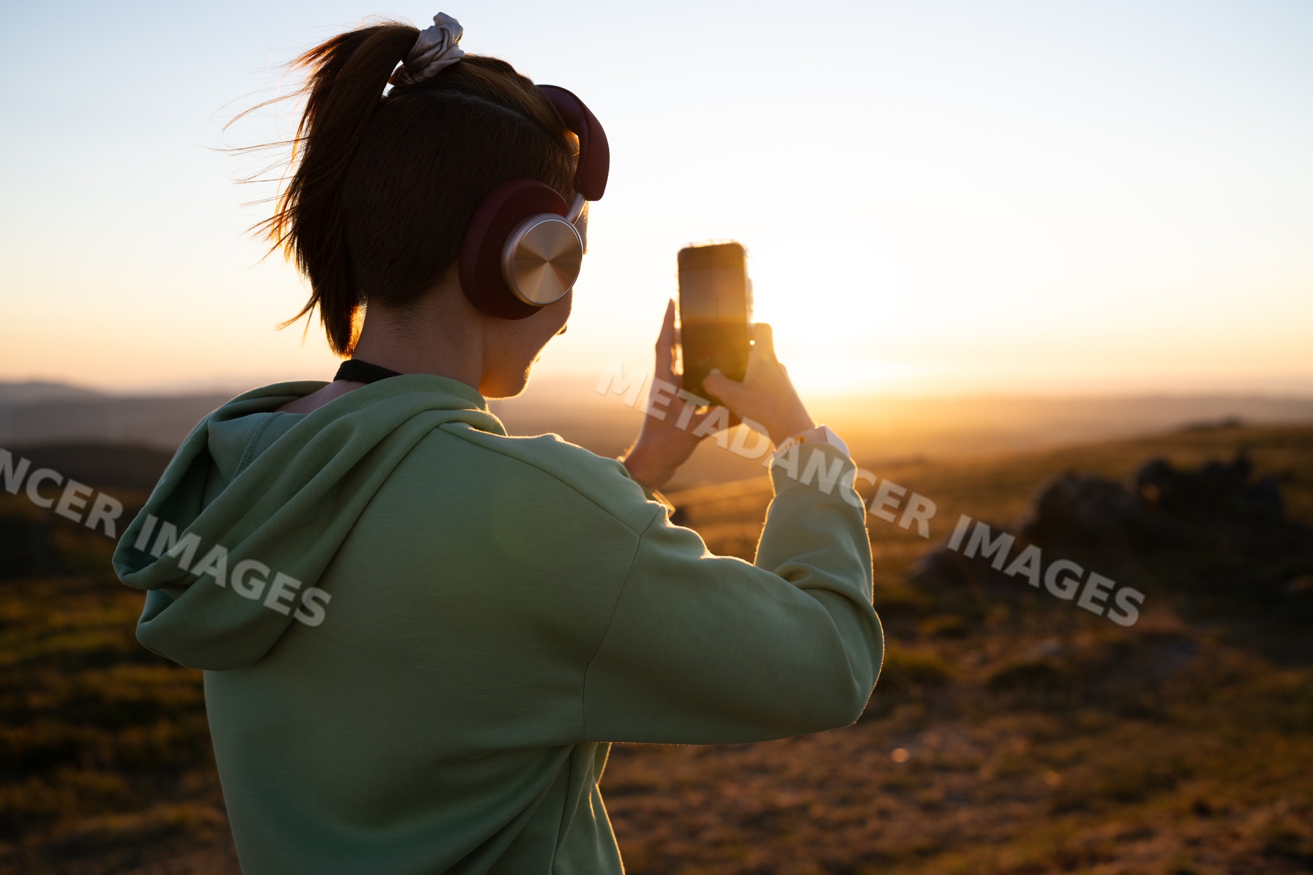 White Woman takes a photo of a sunset landscape outdoors