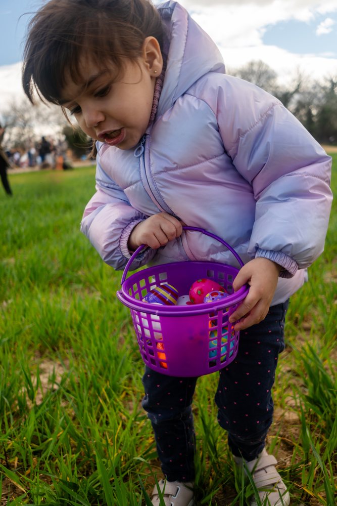 Young white girl holding a basket full of colorful eggs outdoors