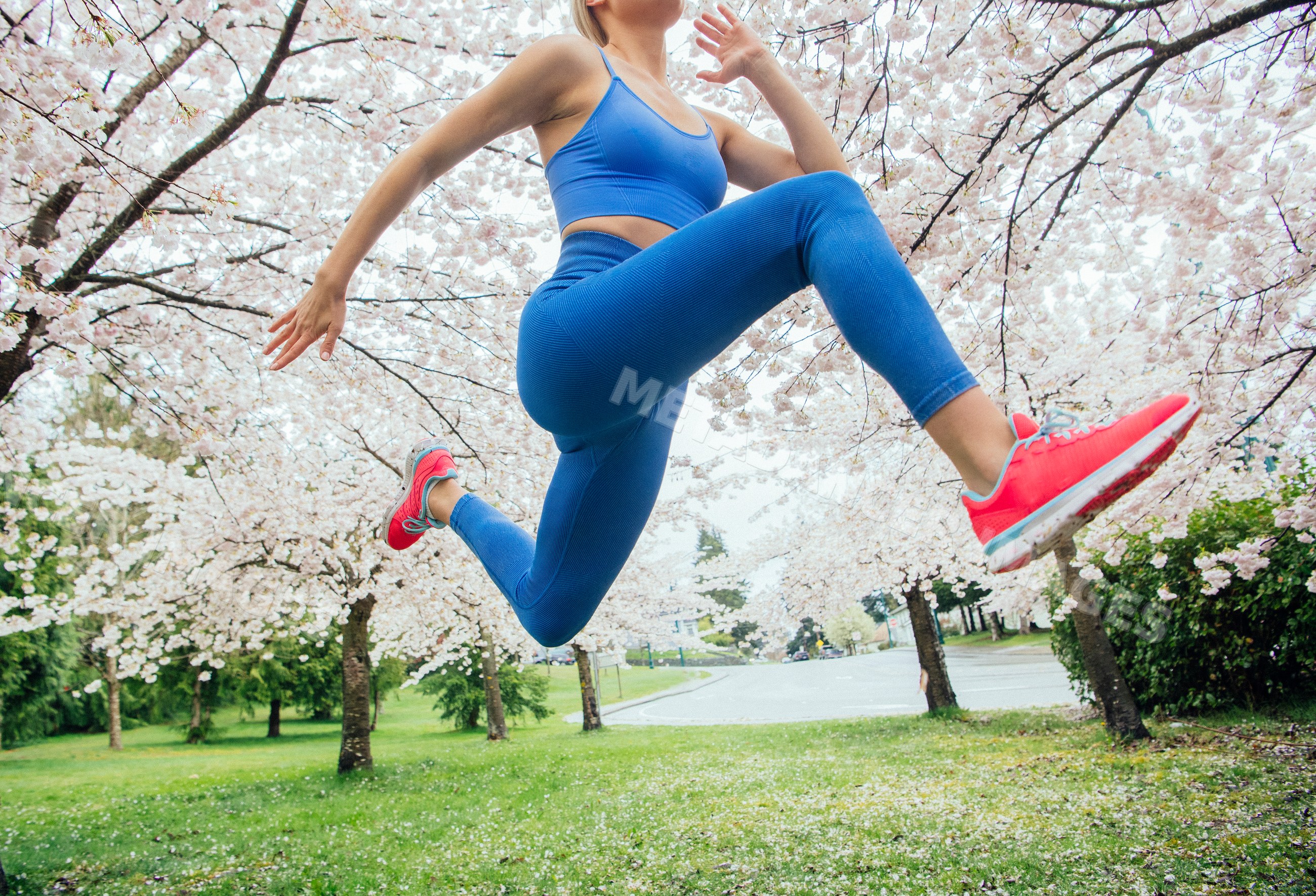 White woman jumping outdoors in a park with cherry blossom trees