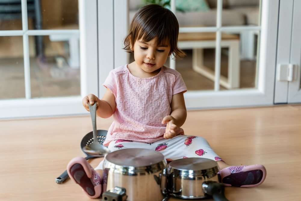 Toddler white girl playing with pots on wooden floor indoors
