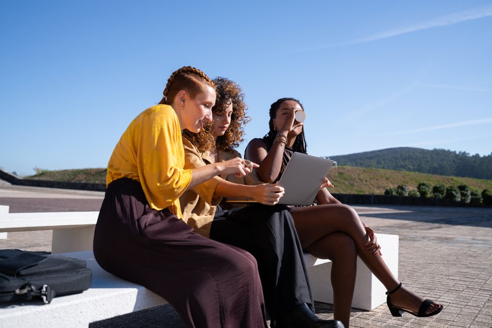 African American and white women using tablet together outdoors