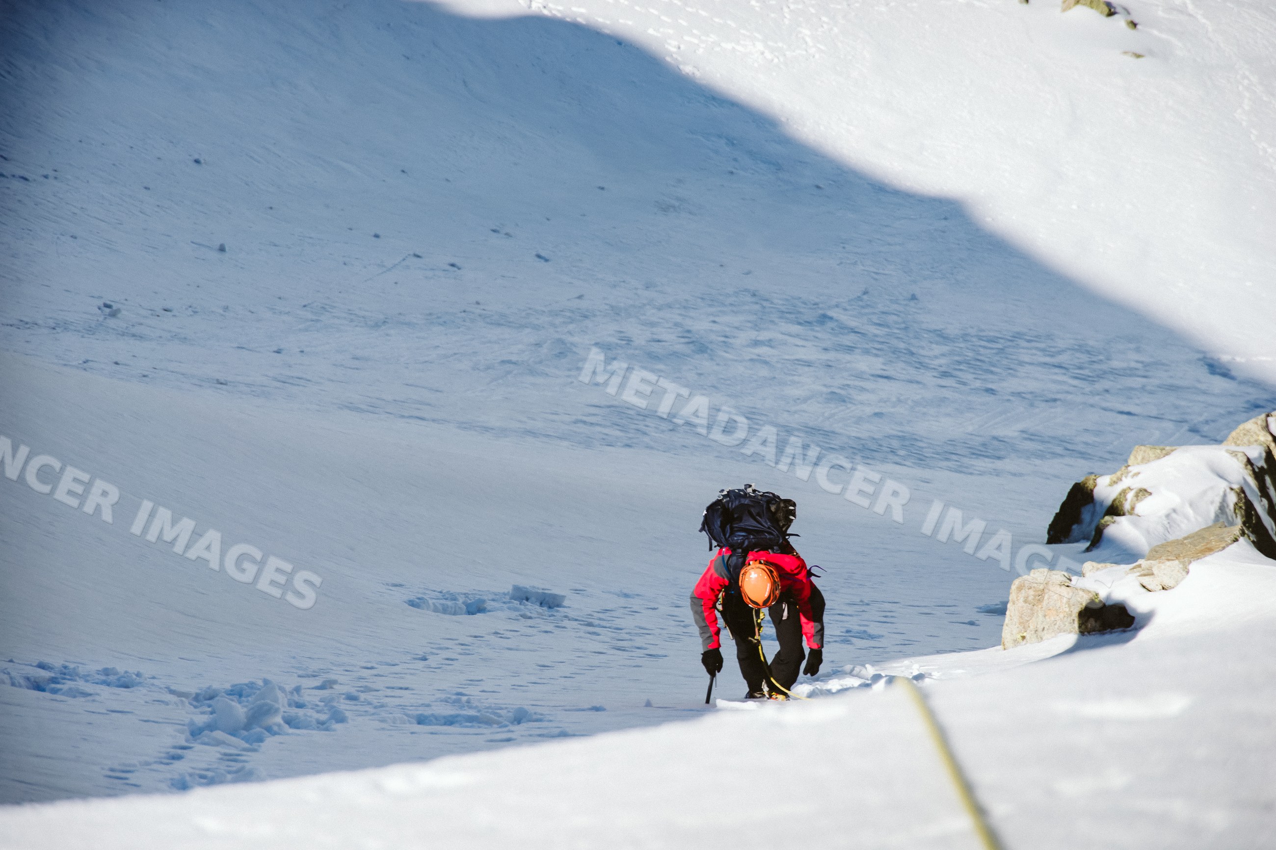 Mountaineer climbing snowy mountain slope with ice axe and rope