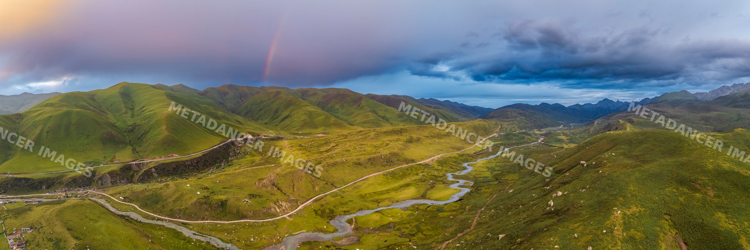 Rainbow over green hills and winding river at sunset in Kham Tibet