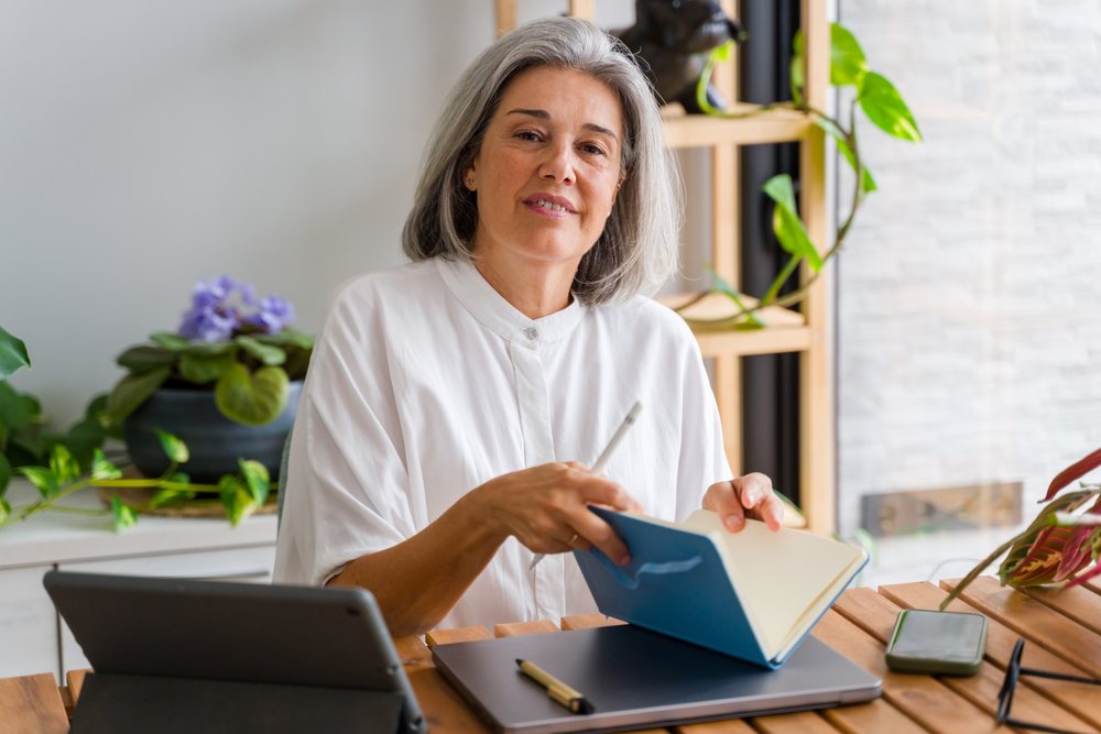 Mature white woman writing in notebook at home workspace in Spain