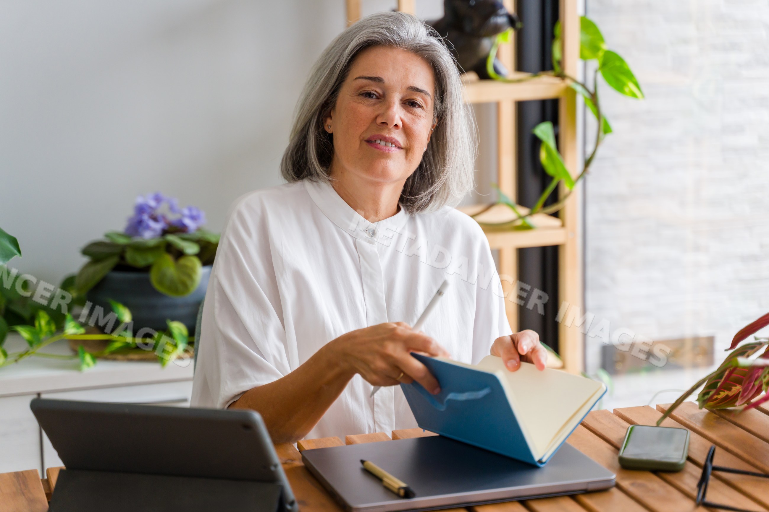 Mature white woman writing in notebook at home workspace in Spain