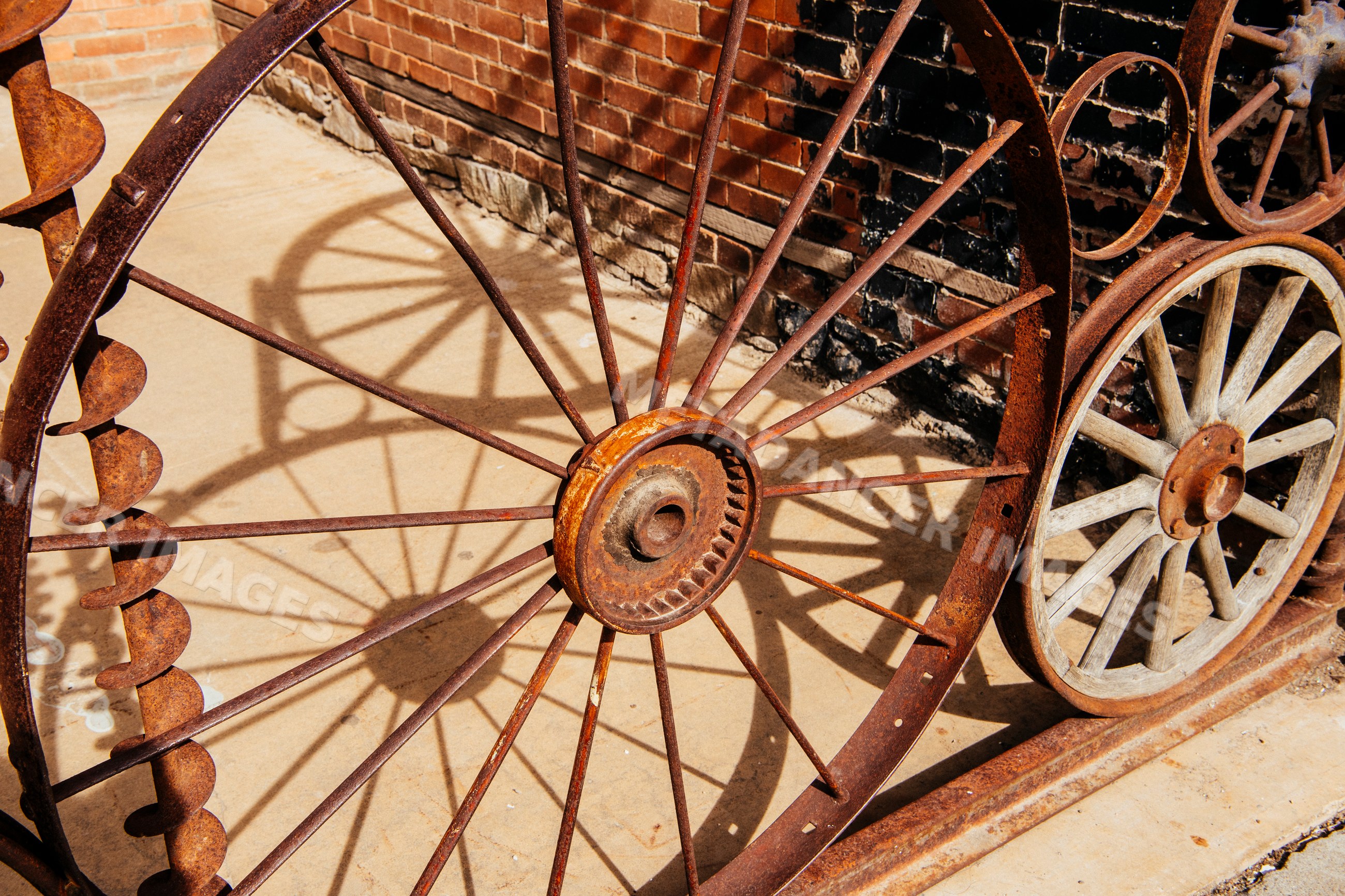 Rusty iron wheels casting shadows on concrete by brick wall