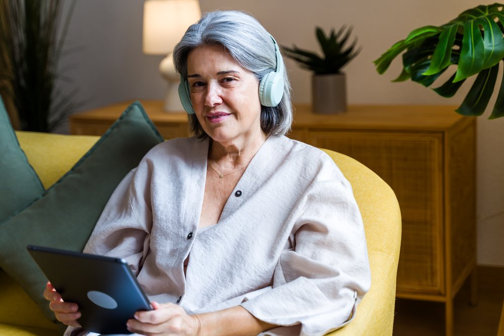 White woman with headphones using tablet on yellow sofa indoors