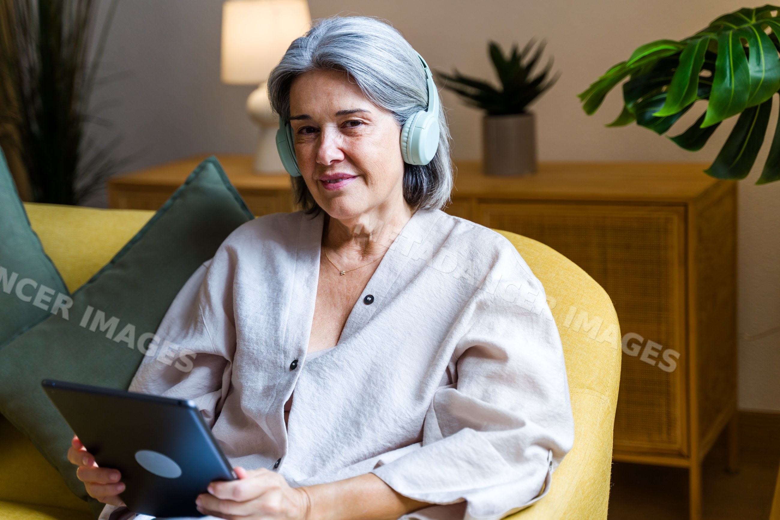 White woman with headphones using tablet on yellow sofa indoors