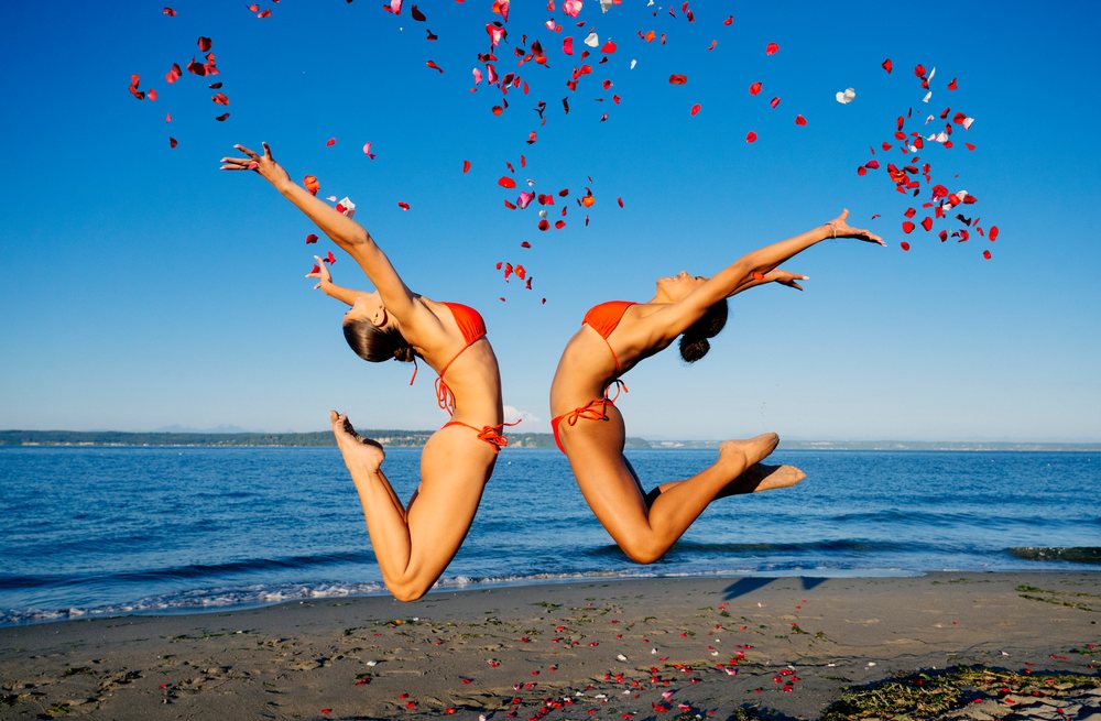 Two women jump on a sunny beach throwing rose petals in wa USA