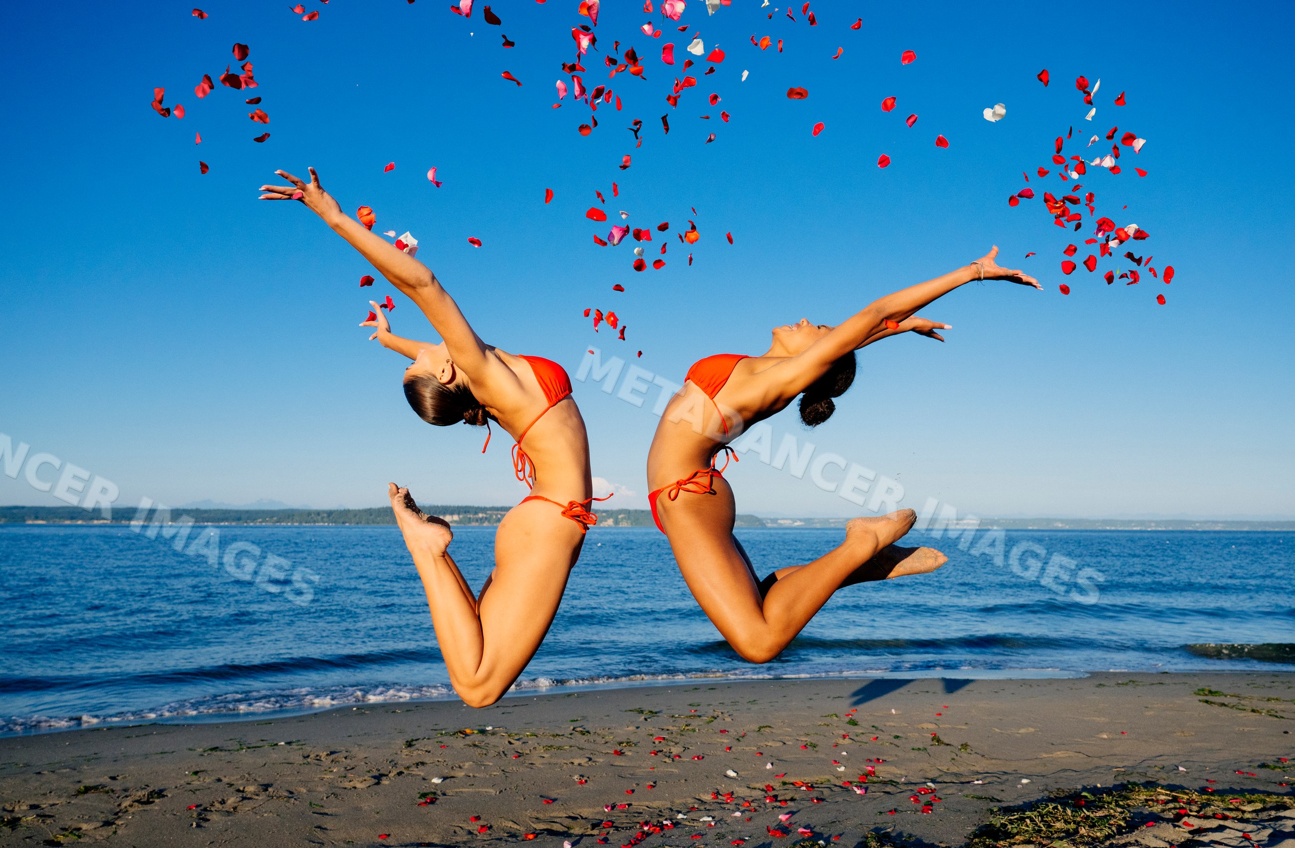Two women jump on a sunny beach throwing rose petals in wa USA
